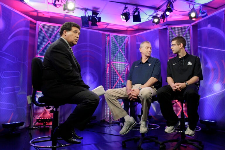 FILE - Greg Gumbel, left, watches as Connecticut head coach Jim Calhoun talks to Butler head coach Brad Stevens, right, prior to taping a television interview for the men's NCAA Final Four college basketball championship game Sunday, April 3, 2011, in Houston. (AP Photo/Eric Gay, File)