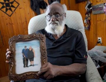 Kenny Pollard sitting in a chair holding up a framed photograph of him and his wife on the beach