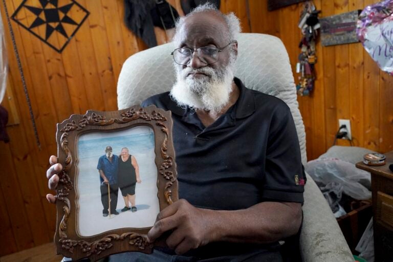 Kenny Pollard sitting in a chair holding up a framed photograph of him and his wife on the beach