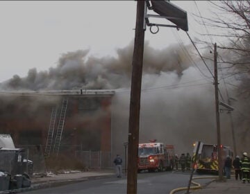 Smoke pours out of a building in front of a group of firefighters