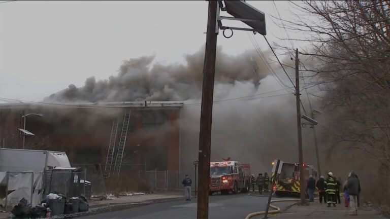 Smoke pours out of a building in front of a group of firefighters