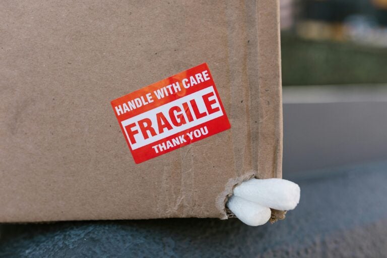 A cardboard box with packing peanuts poking out and a sticker reading HANDLE WITH CARE FRAGILE THANK YOU