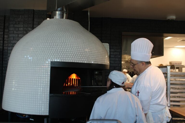 Two chefs put pizza in an oven