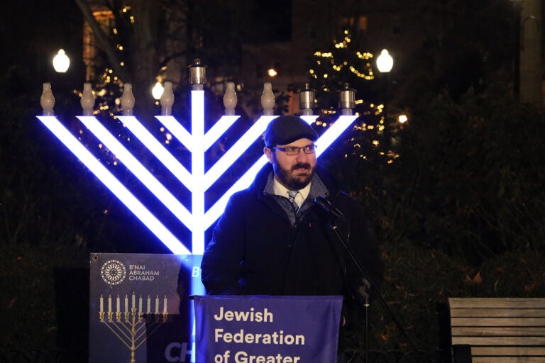 A male rabbi speaks in front of a menorah in Philadelphia