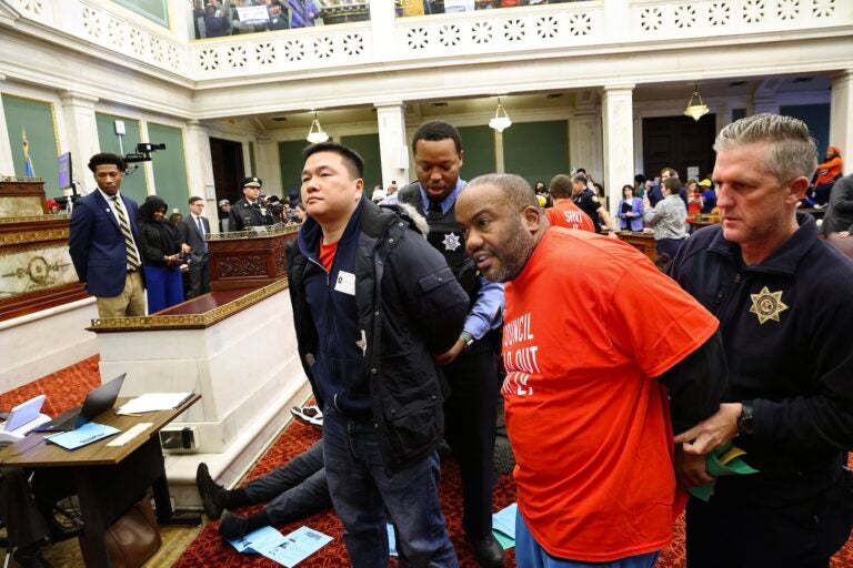 Two protesters being led out of council chambers in handcuffs by police officers