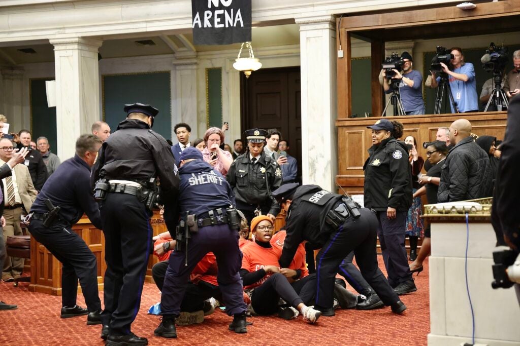 Police officers arresting a group of protesters who are sitting on the floor of council chambers