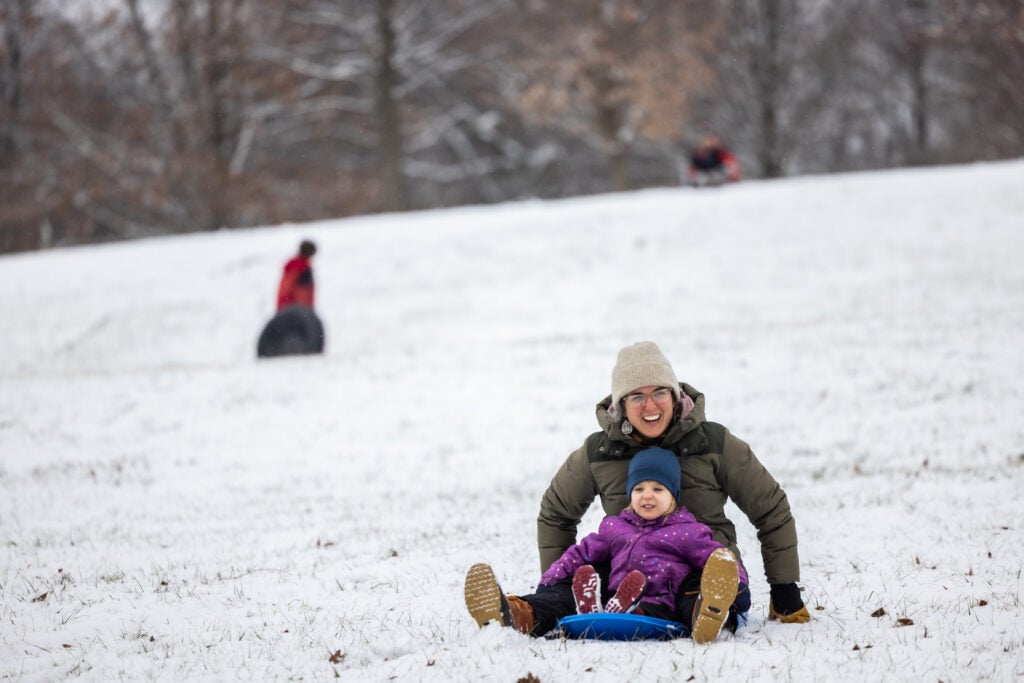 a woman and child sled down a snowy hill