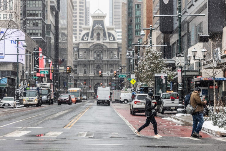 two people cross the street near City Hall