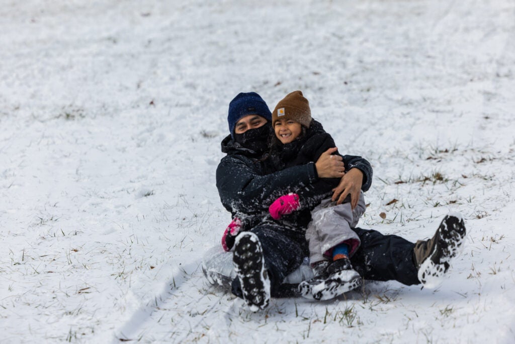 a man and child smile while sledding in the snow