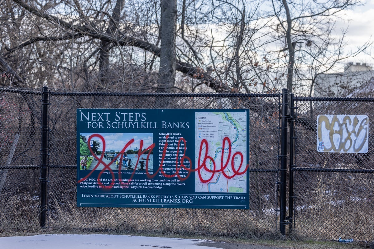 a sign for plans for the trail has graffiti