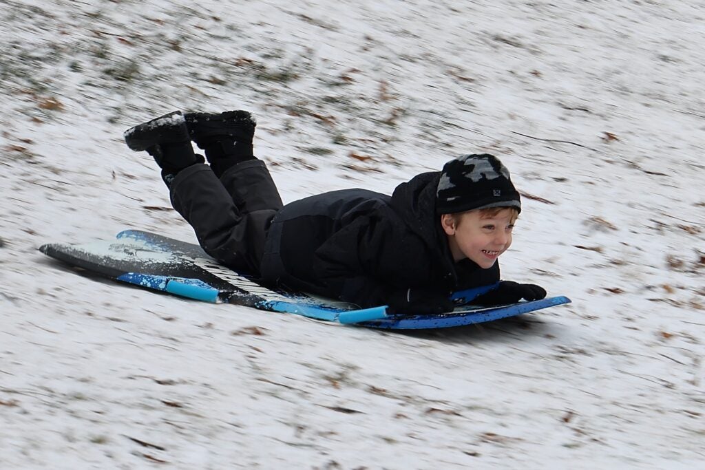 A young child going down a hill head-first on a sled