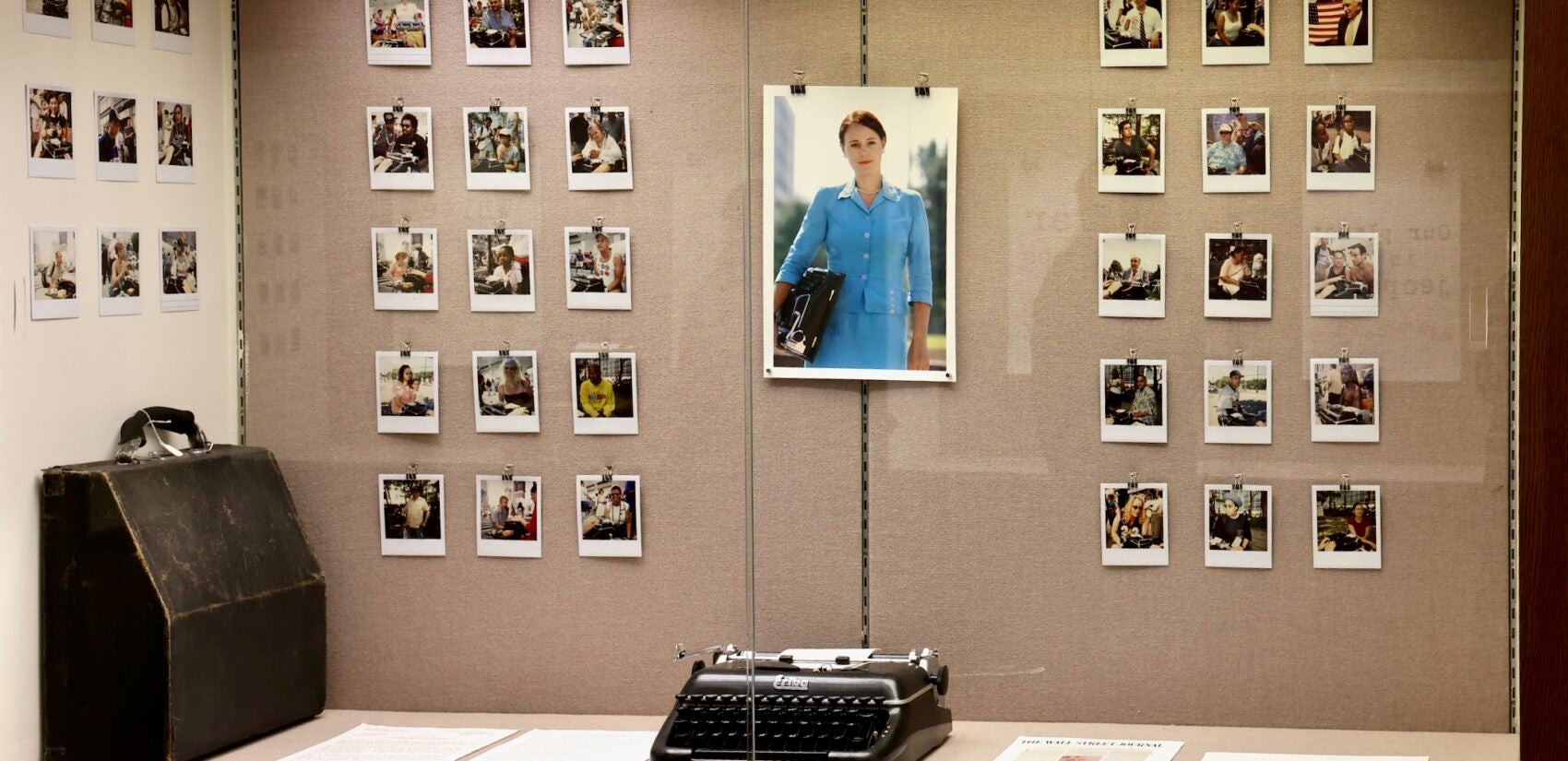 Photos, including a large one of a woman holding a typewriter, hang in a display