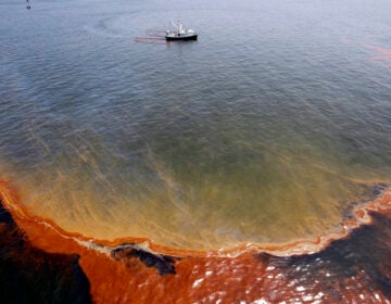 FILE - This Wednesday, May 5, 2010 file picture shows a plume of oil as a shrimp boat uses booms to collect oil in the waters of Chandeleur Sound, La. On April 20, 2010,  a well blew wild under a BP oil platform in the Gulf of Mexico. Eleven workers were missing that day, and would later be declared dead. Ten years after the explosion on that Deepwater Horizon rig off Louisiana's coast, The Associated Press is making the original story and photographs available. (AP Photo/Eric Gay)