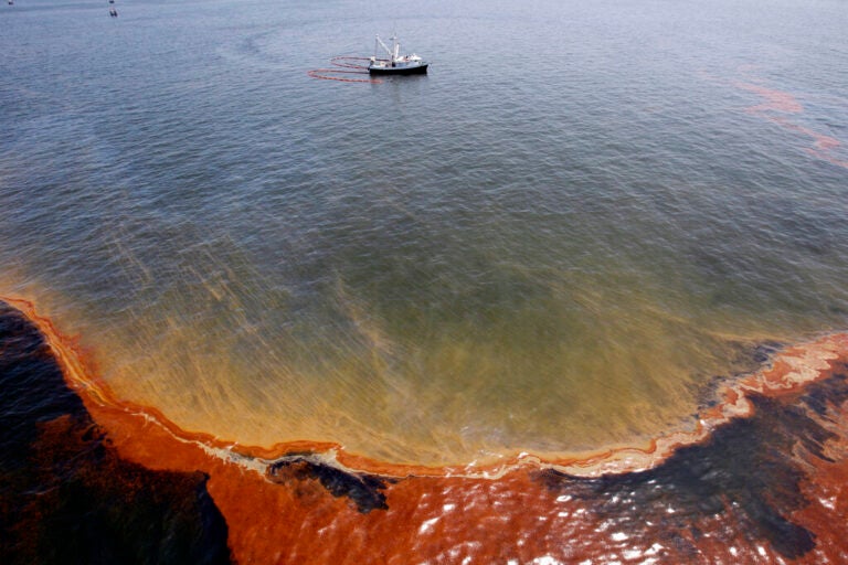 FILE - This Wednesday, May 5, 2010 file picture shows a plume of oil as a shrimp boat uses booms to collect oil in the waters of Chandeleur Sound, La. On April 20, 2010,  a well blew wild under a BP oil platform in the Gulf of Mexico. Eleven workers were missing that day, and would later be declared dead. Ten years after the explosion on that Deepwater Horizon rig off Louisiana's coast, The Associated Press is making the original story and photographs available. (AP Photo/Eric Gay)