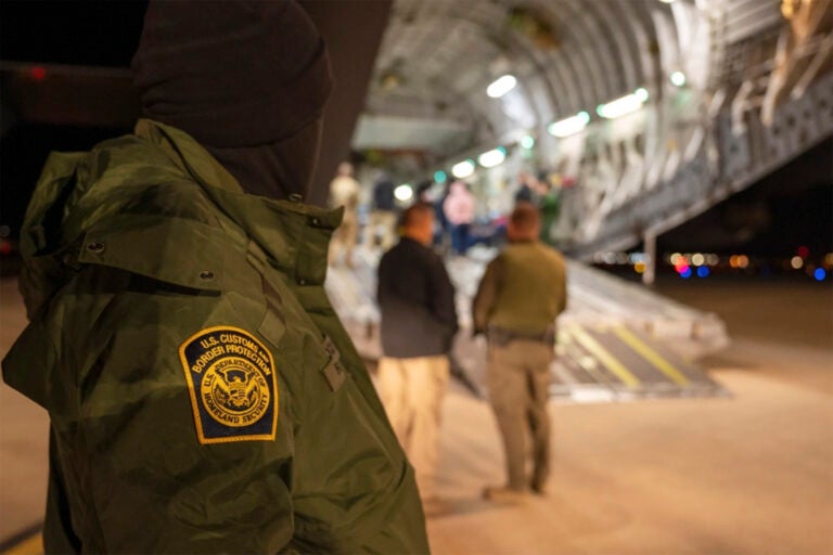 A U.S. Customs and Border Protection agent watches as undocumented immigrants are loaded onto a plane