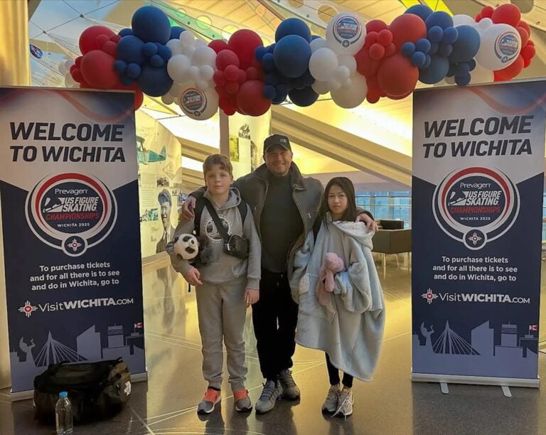 Two child ice skaters stand beside a coach in Kansas