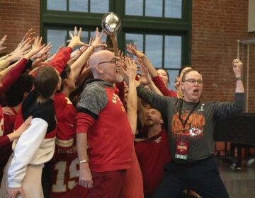 Kansas City Ballet Artistic Director Devon Carney leads a cheer holding the Lombardi trophy with a group of people reaching for it