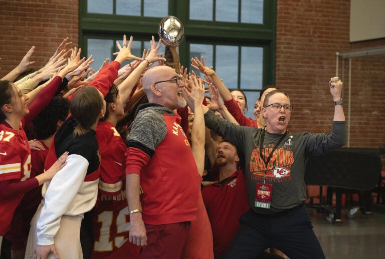 Kansas City Ballet Artistic Director Devon Carney leads a cheer holding the Lombardi trophy with a group of people reaching for it