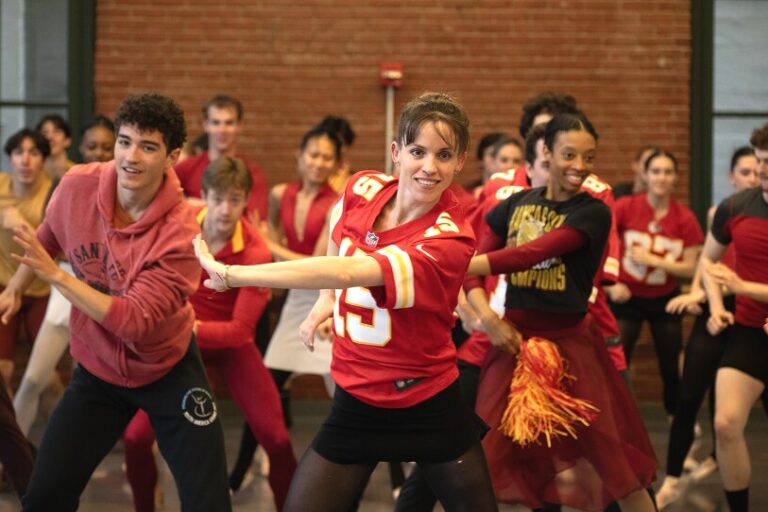 A woman wearing a Kansas City Chiefs jersey leads a dance sequence with other dancers behind her