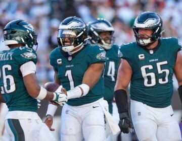 Jalen Hurts hands the ball to Saquon Barkley while Lane Johnson looks on