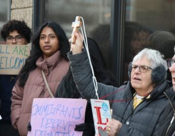 Protesters hold a cross and signs reading ALL ARE WELCOME and IMMIGRANTS DESERVE DIGNITY