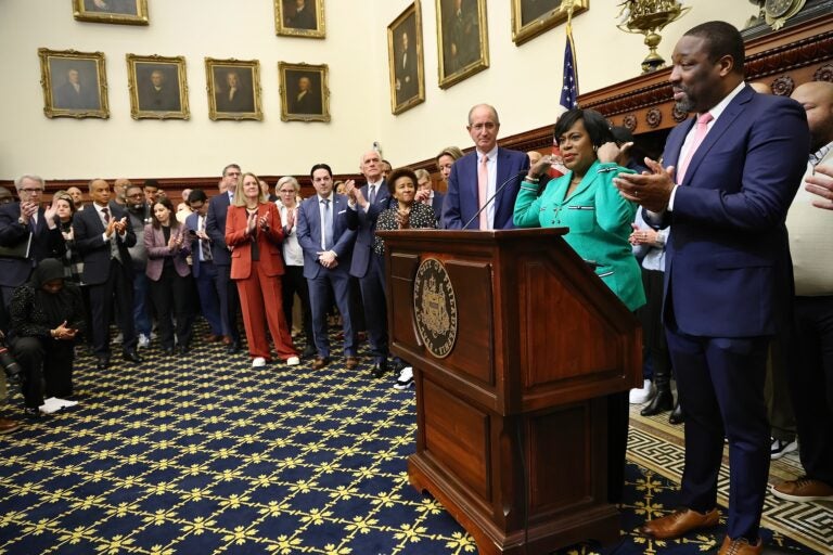 Mayor Parker speaks behind a podium next to Kenyatta Johnson and Josh Harris