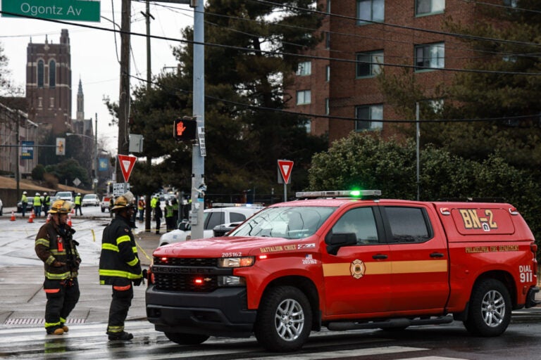 A fire department car parked in the street with two firefighters nearby