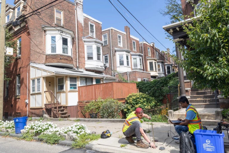 two researchers hammering into the ground outside rowhouses