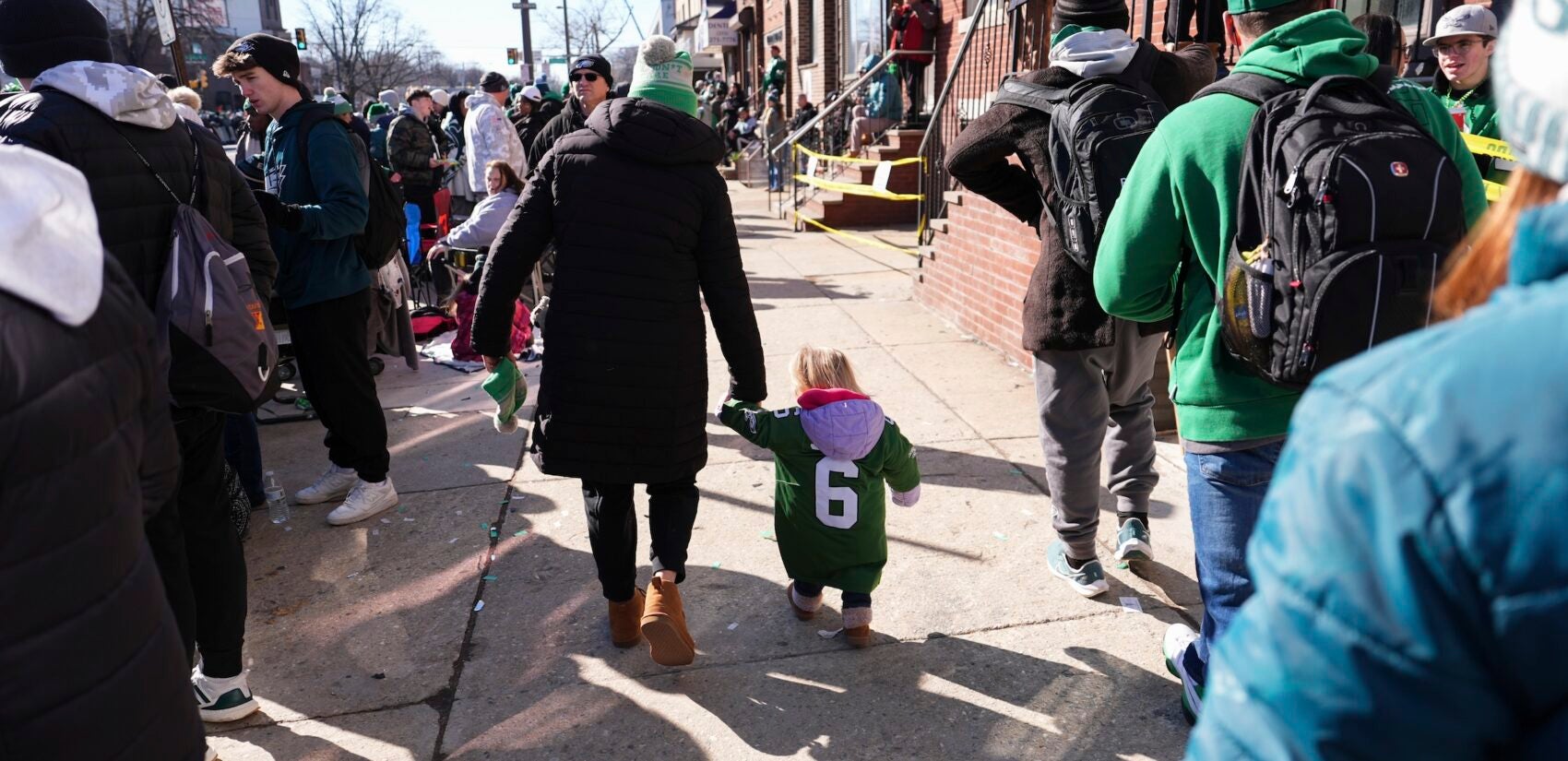 A small child walking with their parent along the parade route