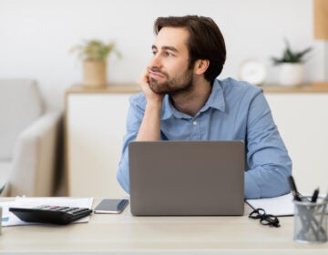 A bored businessman sitting at a laptop, procrastinating at work. (Photo Courtesy/Bigstock)