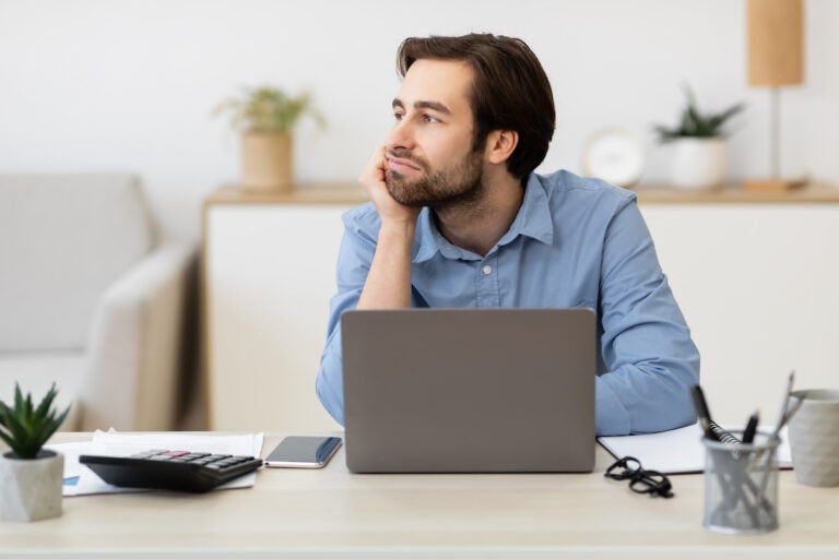 A bored businessman sitting at a laptop, procrastinating at work. (Photo Courtesy/Bigstock)