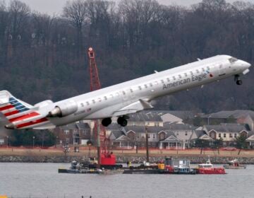 Crews recover wreckage from the crash as another plane takes off overhead