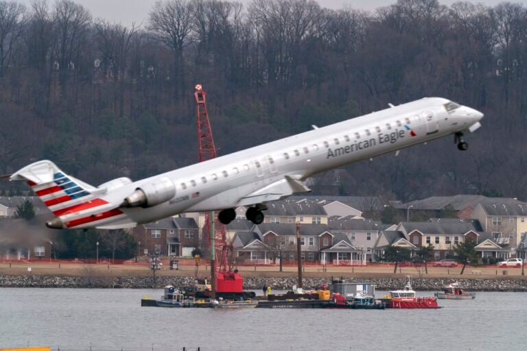 Crews recover wreckage from the crash as another plane takes off overhead