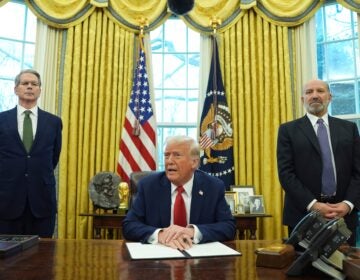 Donald Trump sitting while Scott Bessent and Howard Lutnick stand