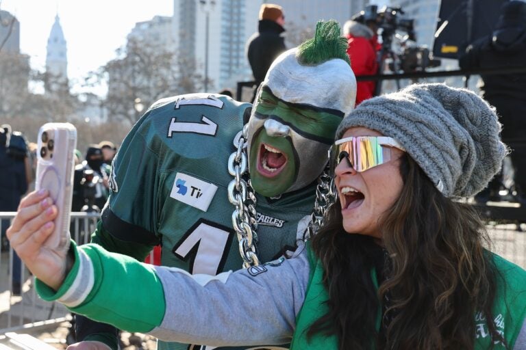 A woman takes a selfie posing with a guy in full face-paint and mohawk and eagles jersey