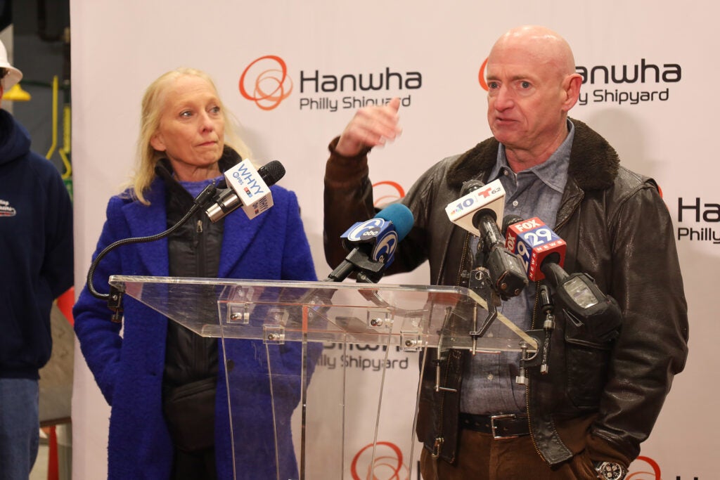 Mark Kelly speaking at a podium with Mary Gay Scanlon standing beside him