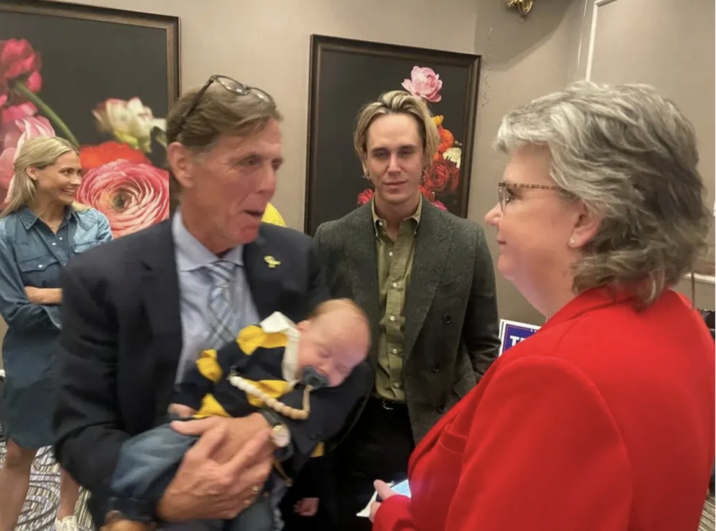 Mike Ramone holding a baby, and speaking to Julianne Murray