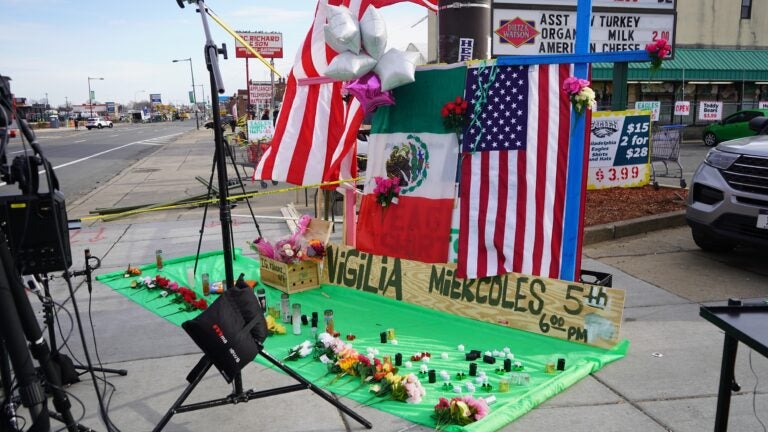 a memorial on the sidewalk for Nigilia Miekcoles 5th, with flags, flowers and candles