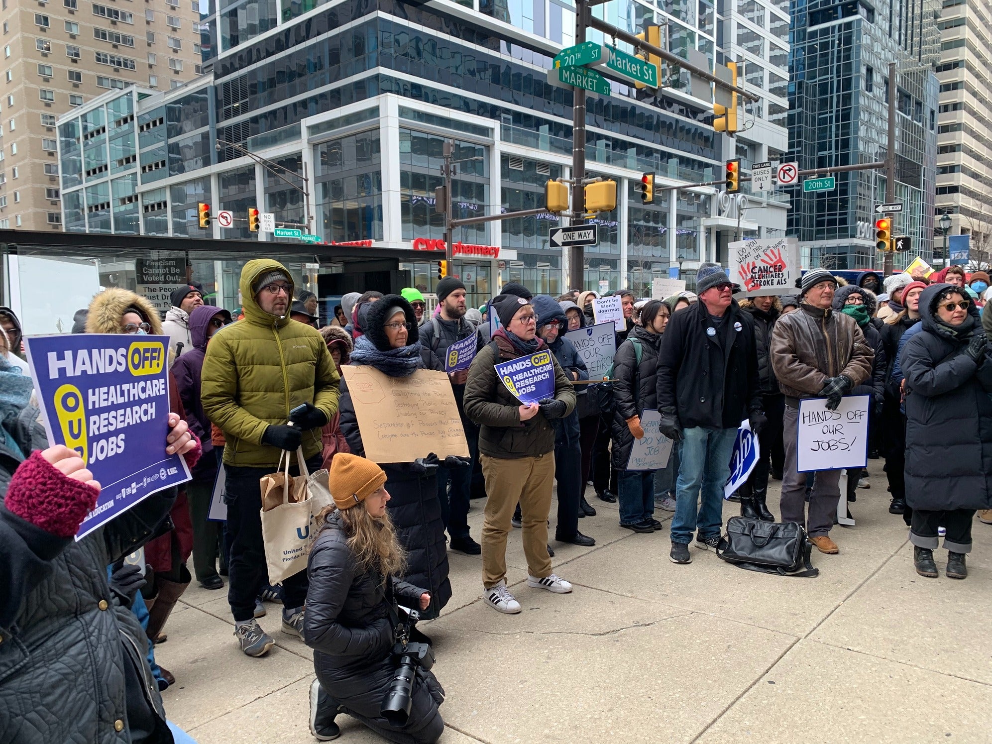 people protesting with signs reading HANDS OFF OUR JOBS! and HANDS OFF OUT HEALTHCARE RESEARCH JOBS