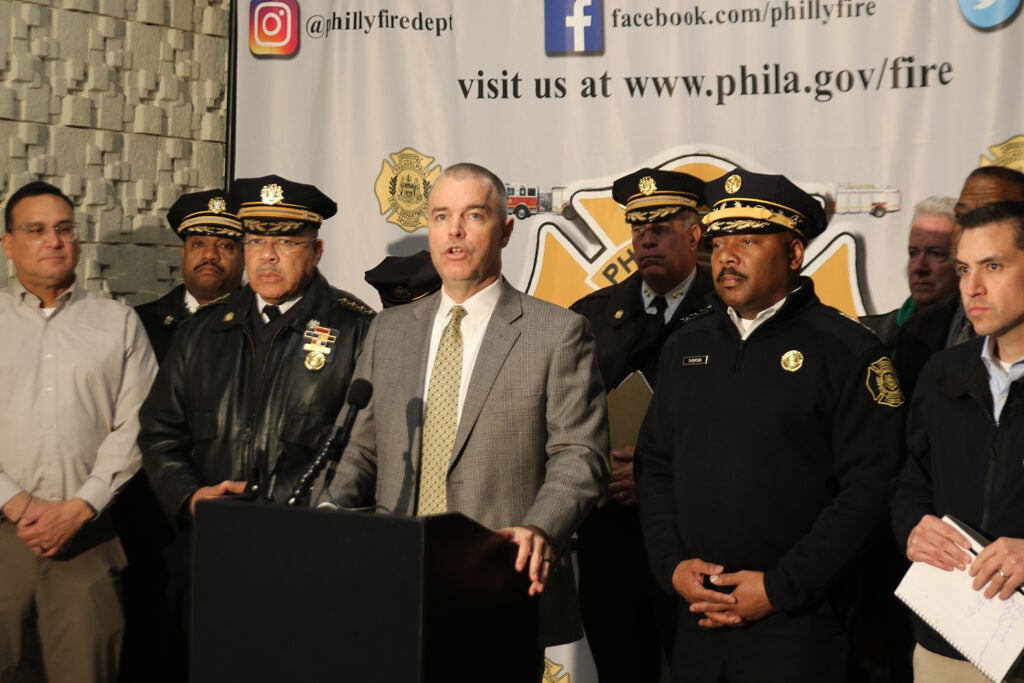 Philadelphia Managing Director speaks on a podium surrounded by emergency personnel to talk about Northeast Philadelphia aircraft accident