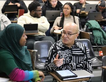 A man in a college classes talks with a female student to his right