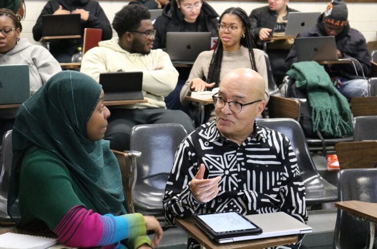 A man in a college classes talks with a female student to his right