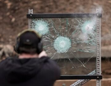 A man shooting a gun at a piece of bulletproof glass as a test