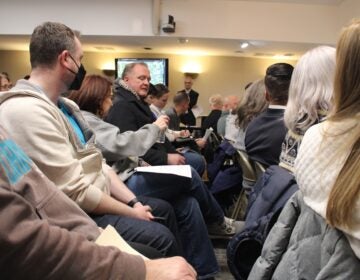 People at a town hall meeting passing a bottle of water around so they can smell it.