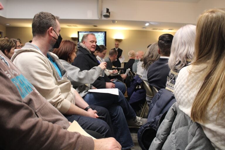 People at a town hall meeting passing a bottle of water around so they can smell it.