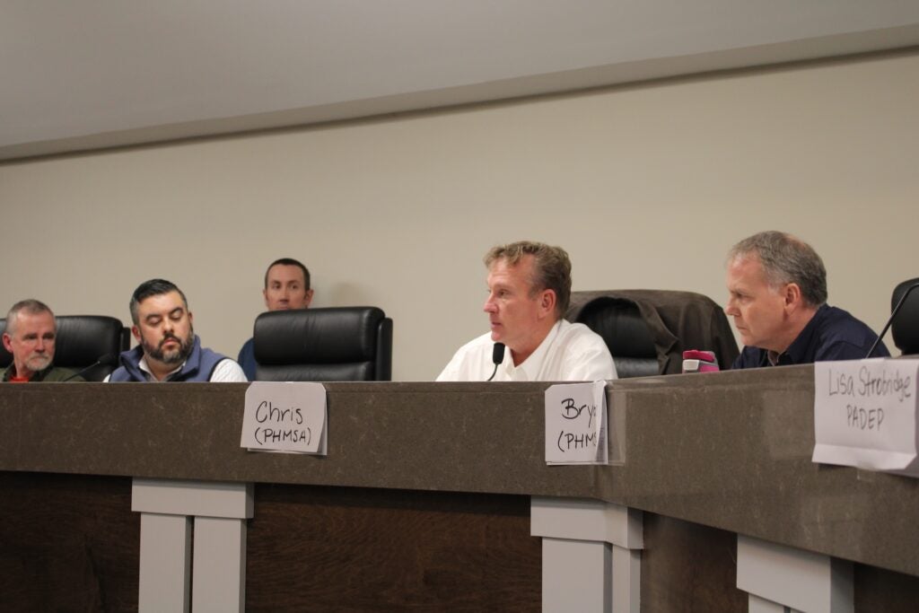 Officials sitting at a long desk during a town hall meeting