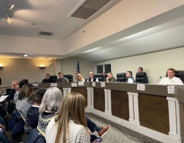 Officials sitting at a long desk during a town hall meeting