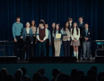 A group of children stand on a stage addressing adults in the audience