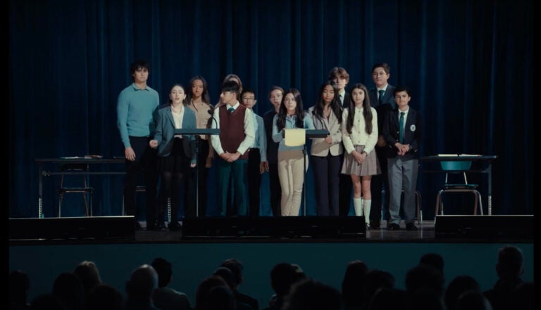 A group of children stand on a stage addressing adults in the audience