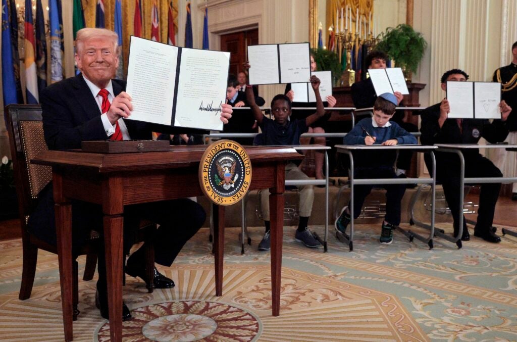 Trump showing the executive order he signed, with school children in the background